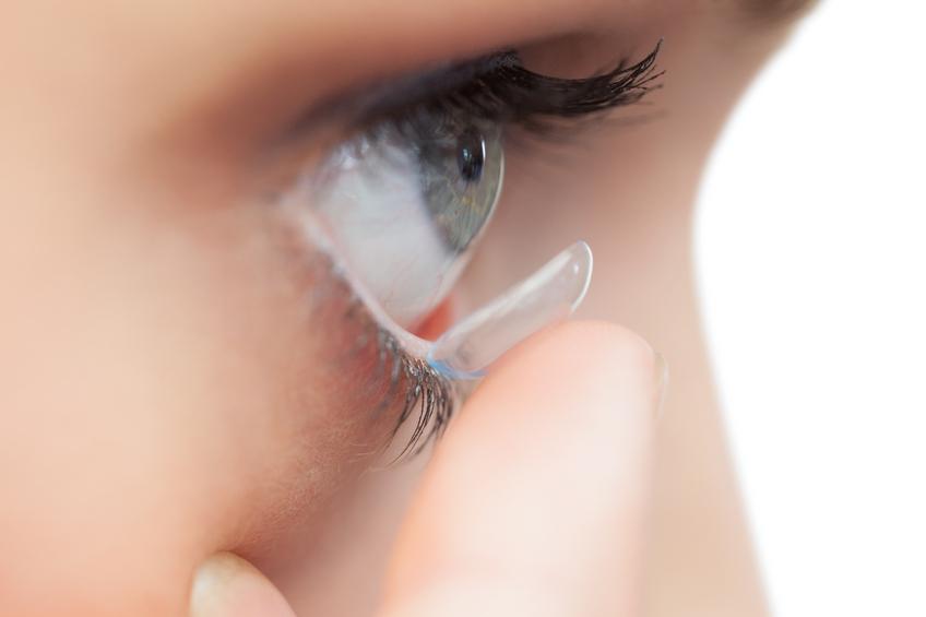 Extreme close up on young model applying contact lens on her blue eyes