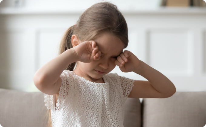 niña con camisa blanca frotándose los ojos