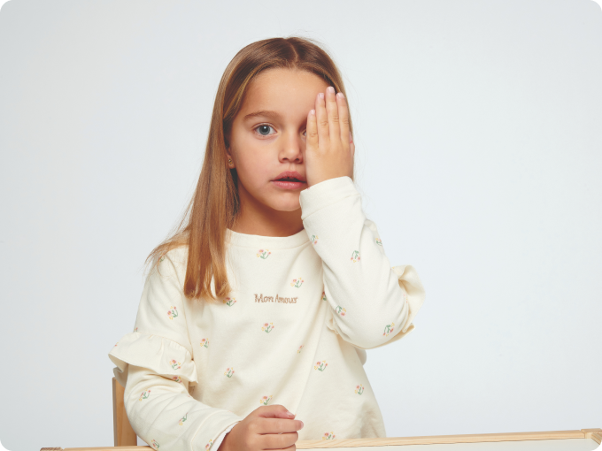 niña rubia sentada en mesa tapándose un ojo