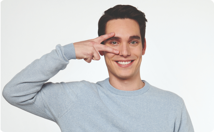 hombre joven con jersey gris haciendo la señal de la victoria sobre un ojo