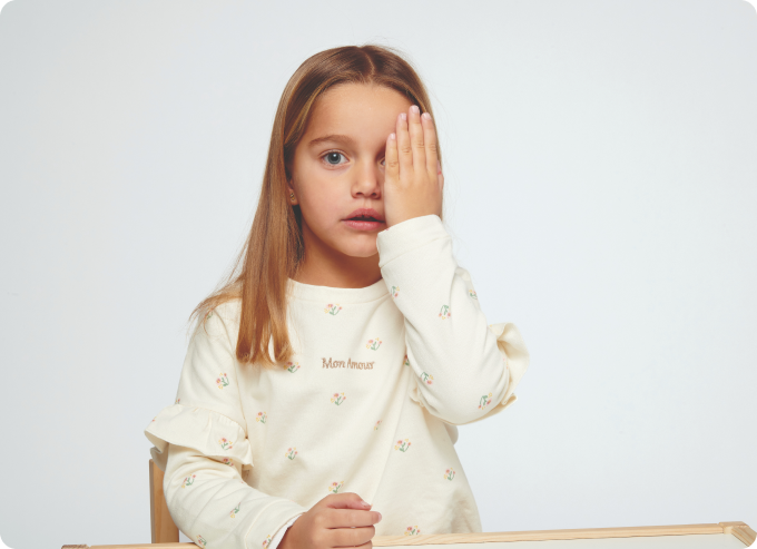 niña rubia sentada en mesa tapándose un ojo